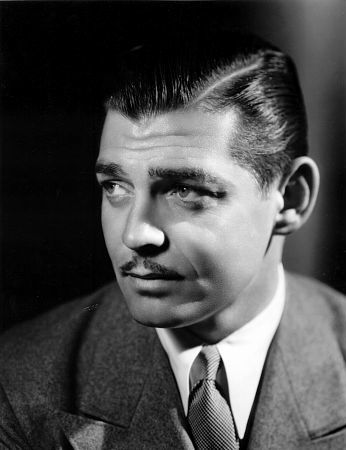 Photo of Clark Gable at his peak, probably in 'Gone with the Wind.' His hair is sleek with gel, his eyes are melancholy and gazing off into the distance, and his jaw is set. He looks very serious and handsome.