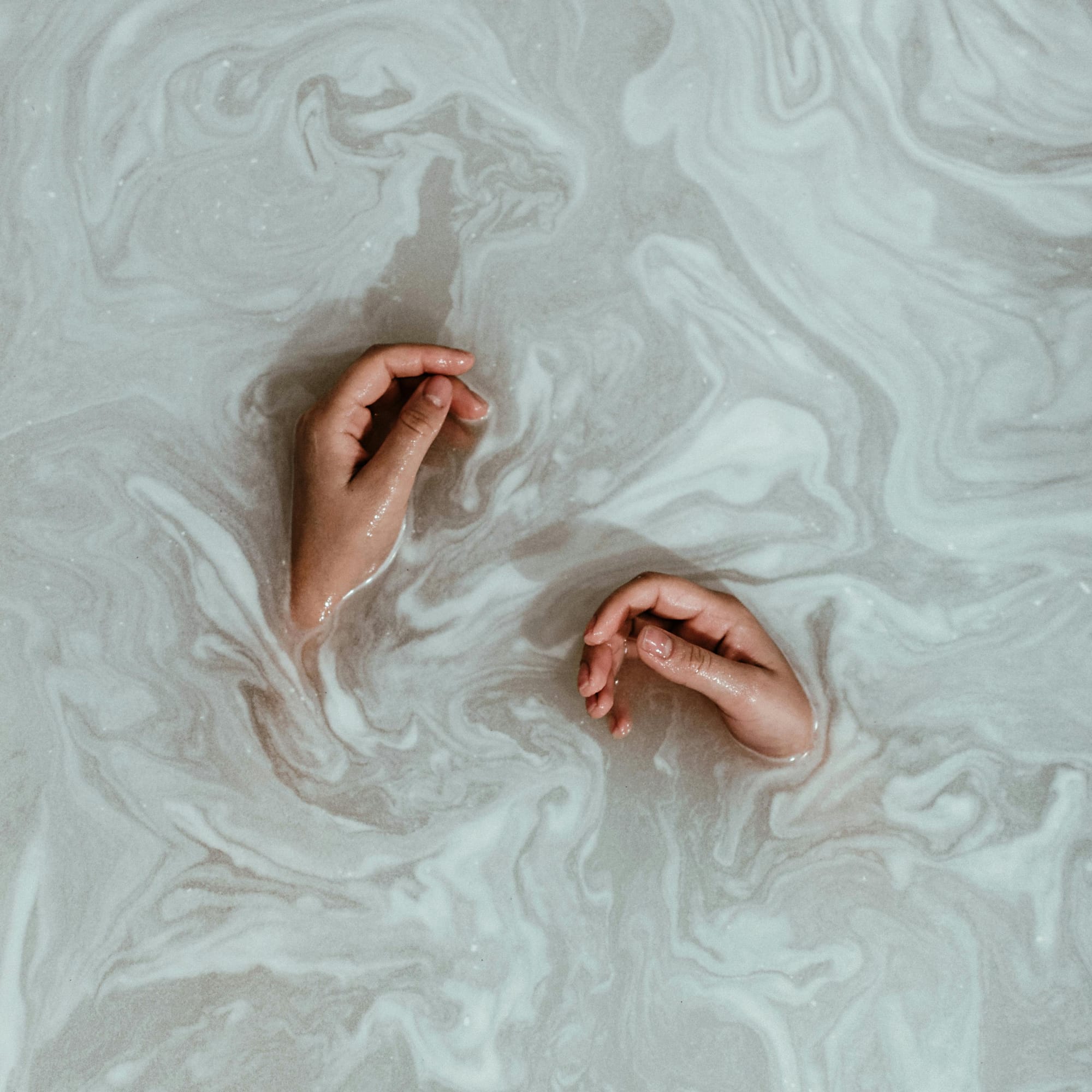 A pair of hands half submerged in swirls of soapy bathwater