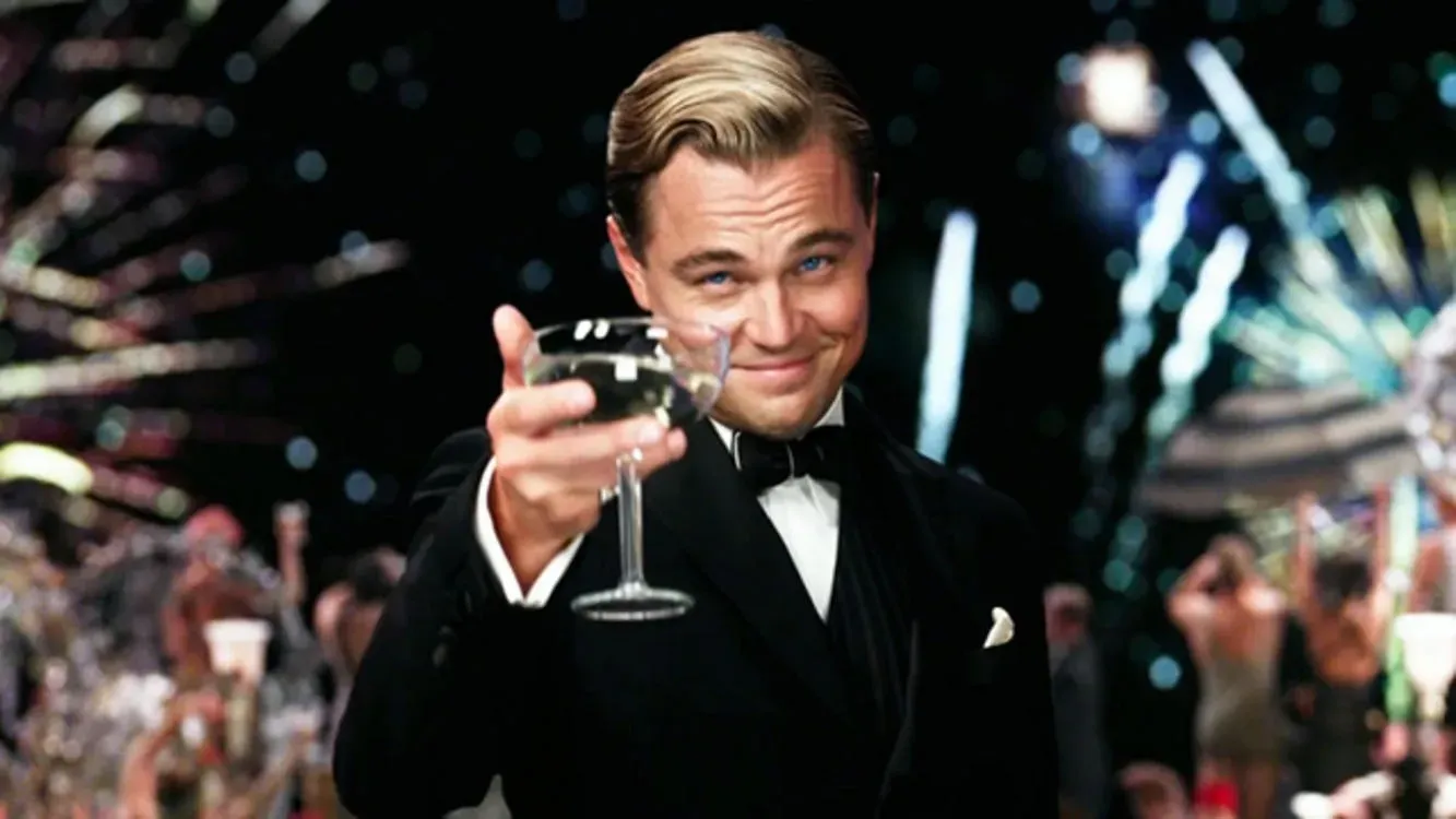 Leonardo DiCaprio as Jay Gatsby holding up a glass of wine in toast