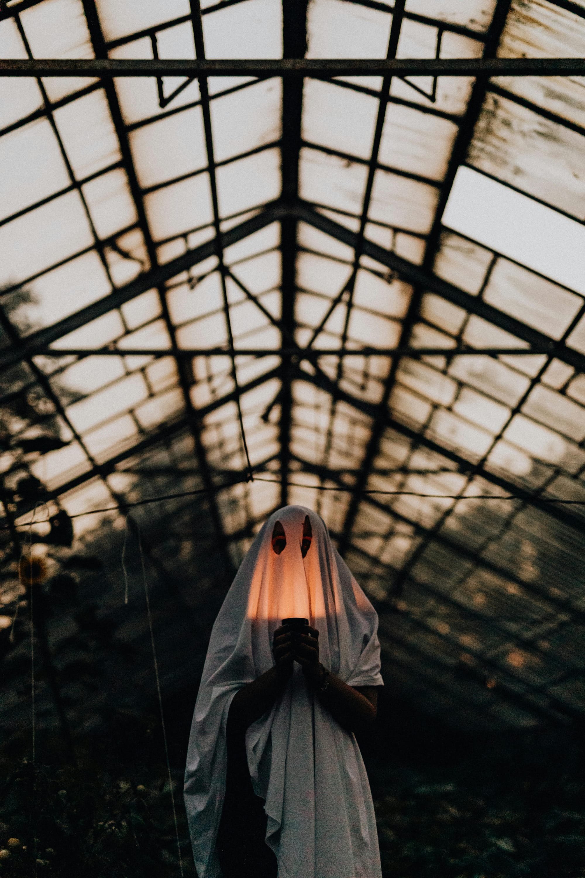 Person in a white sheet with black eye cut outs to look like a ghost, holding up a candle that illuminates the face
